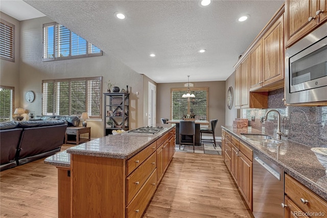 kitchen with stainless steel appliances, backsplash, a kitchen island, a sink, and light wood finished floors