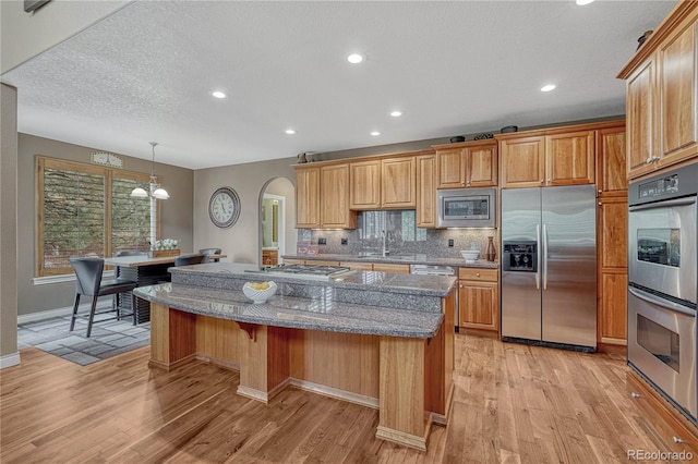kitchen with a center island, decorative backsplash, arched walkways, light wood-style flooring, and appliances with stainless steel finishes