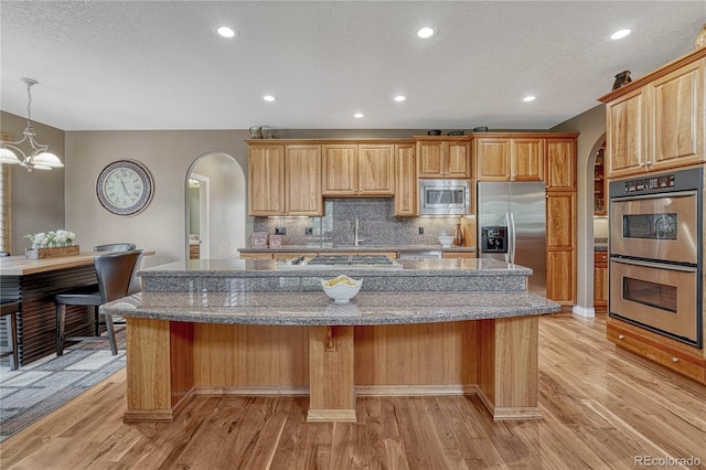 kitchen featuring arched walkways, stainless steel appliances, a center island, and light wood finished floors