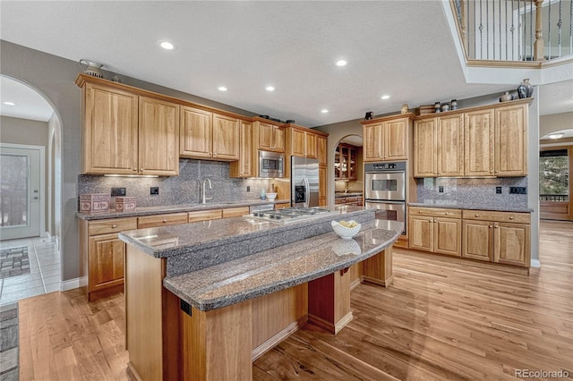 kitchen with light wood-style floors, appliances with stainless steel finishes, a center island, dark stone countertops, and arched walkways
