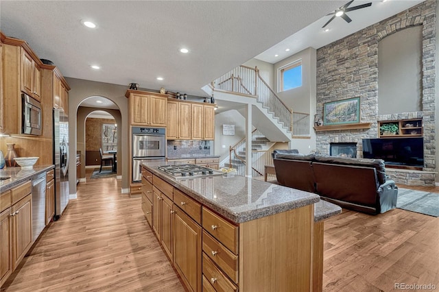 kitchen featuring a kitchen island, appliances with stainless steel finishes, arched walkways, light wood-type flooring, and open floor plan