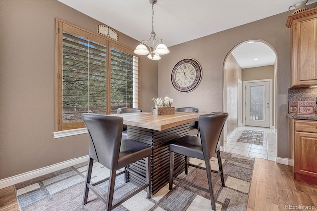 dining space with arched walkways, light wood-style flooring, baseboards, and a notable chandelier