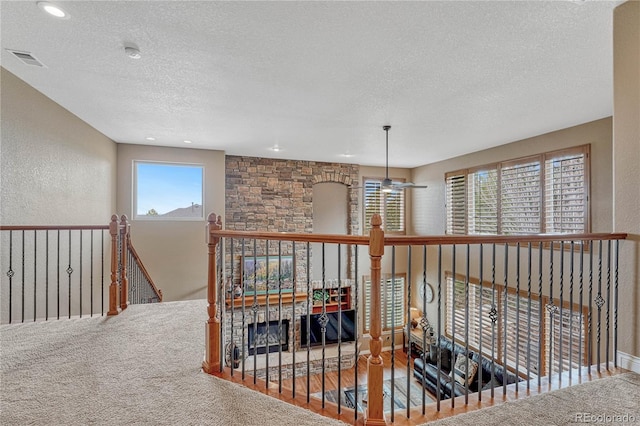 hallway featuring visible vents, carpet, a textured wall, and a textured ceiling