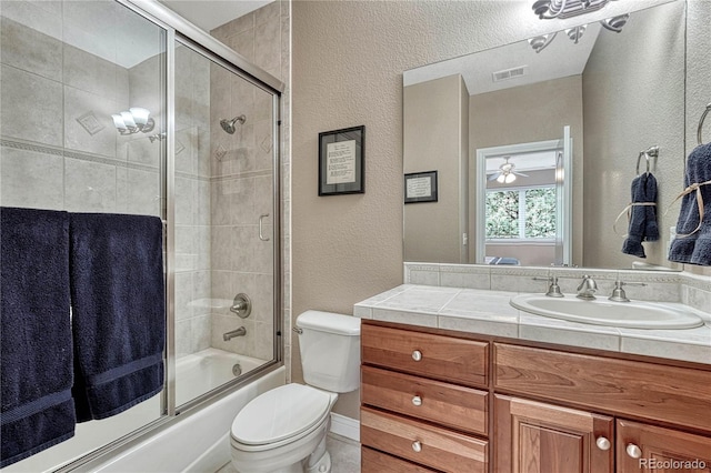 full bathroom with toilet, vanity, enclosed tub / shower combo, visible vents, and a textured wall