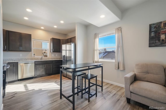 kitchen featuring dark brown cabinetry, light stone counters, light hardwood / wood-style flooring, and appliances with stainless steel finishes