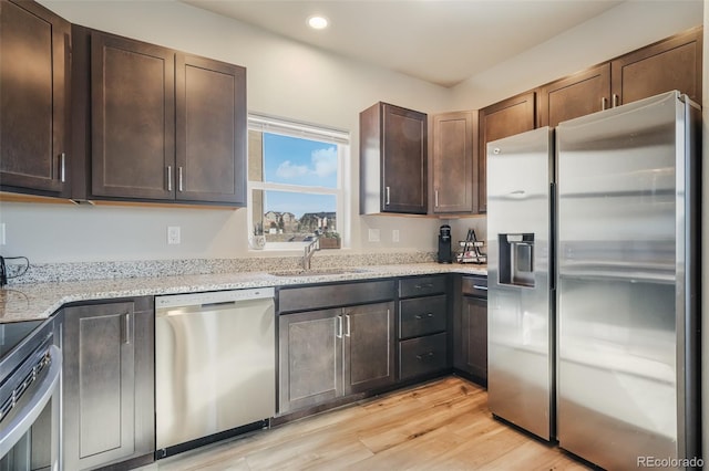 kitchen with sink, dark brown cabinets, stainless steel appliances, light stone counters, and light hardwood / wood-style floors