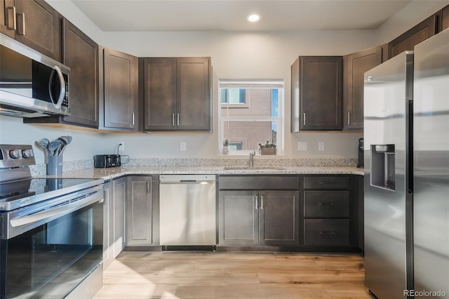 kitchen featuring stainless steel appliances, dark brown cabinets, sink, and light stone counters