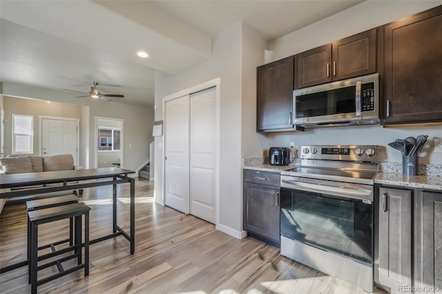 kitchen featuring light stone counters, appliances with stainless steel finishes, light hardwood / wood-style floors, and dark brown cabinets