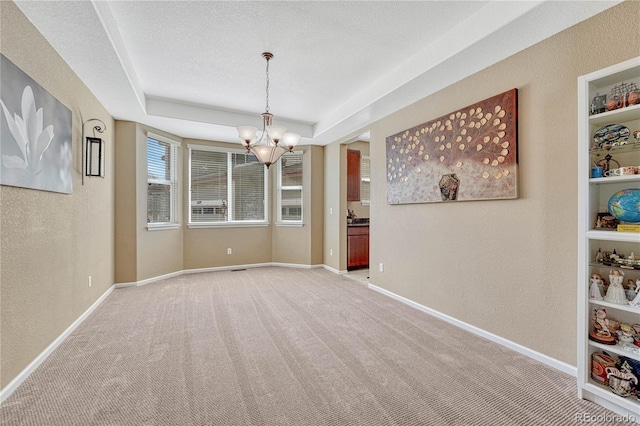 unfurnished dining area featuring a raised ceiling, a notable chandelier, a textured wall, and a textured ceiling