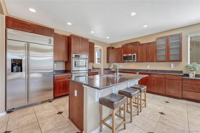 kitchen with a sink, dark stone countertops, a kitchen breakfast bar, stainless steel appliances, and glass insert cabinets