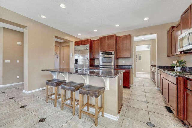 kitchen with a center island with sink, recessed lighting, a kitchen breakfast bar, dark stone countertops, and stainless steel appliances