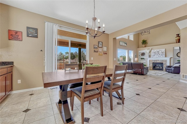 dining area with light tile patterned floors, a healthy amount of sunlight, a fireplace, and an inviting chandelier