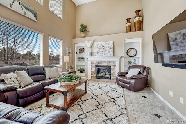 living room with built in features, baseboards, a high ceiling, a stone fireplace, and tile patterned floors