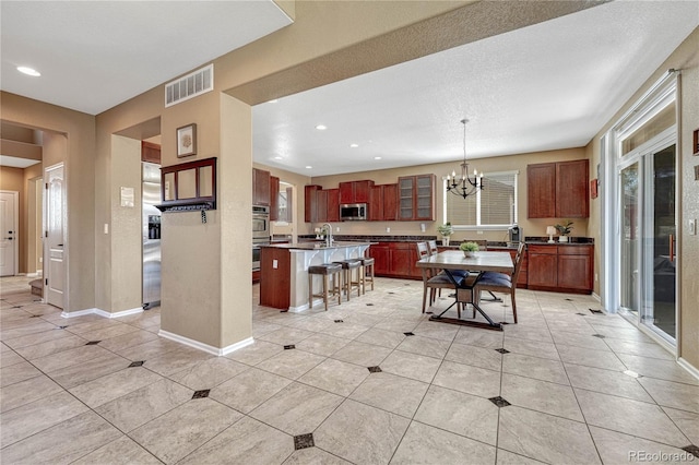 kitchen with visible vents, a kitchen bar, an inviting chandelier, stainless steel appliances, and a kitchen island with sink