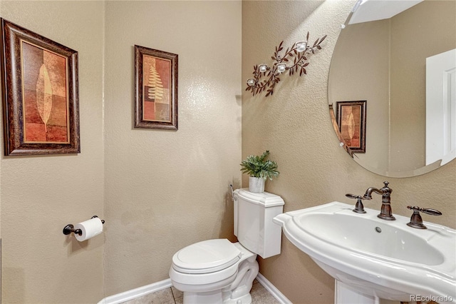 bathroom featuring toilet, a sink, tile patterned flooring, baseboards, and a textured wall