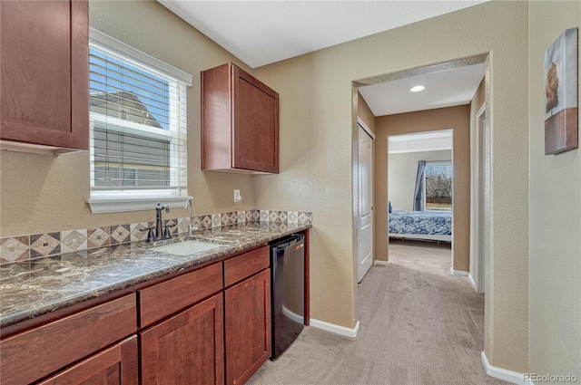 kitchen featuring baseboards, a sink, black dishwasher, light colored carpet, and brown cabinets