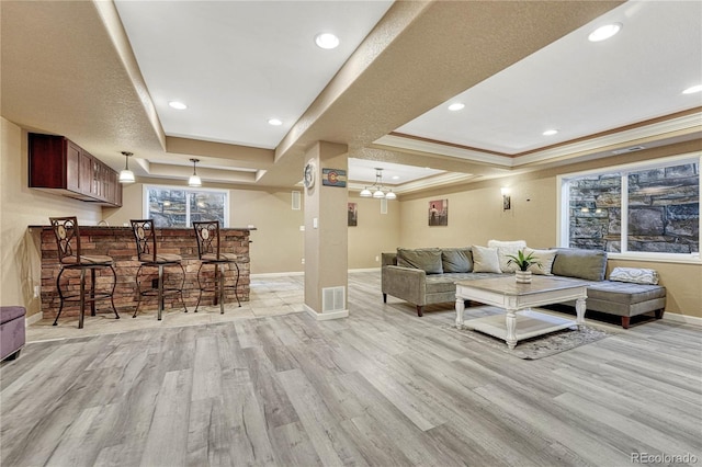 living area featuring visible vents, light wood finished floors, baseboards, crown molding, and a raised ceiling