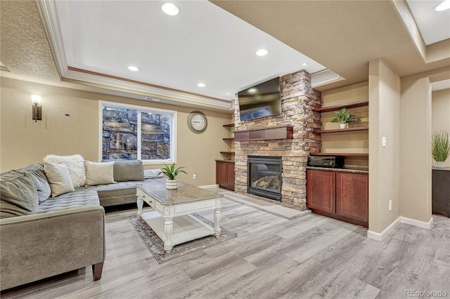 living room with light wood finished floors, a stone fireplace, a raised ceiling, and ornamental molding