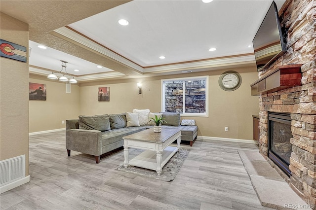 living room featuring a tray ceiling, visible vents, light wood-type flooring, and a stone fireplace