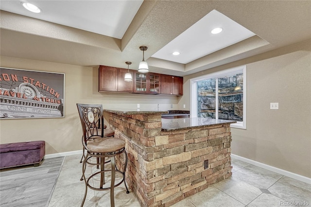 bar with decorative light fixtures, baseboards, a raised ceiling, and indoor wet bar