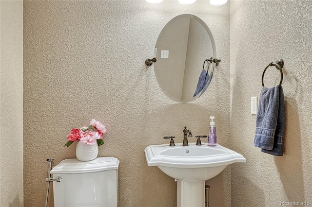 half bathroom with toilet, a textured wall, and a sink