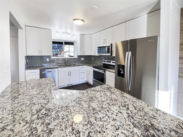 kitchen with appliances with stainless steel finishes, light stone counters, white cabinets, decorative backsplash, and sink