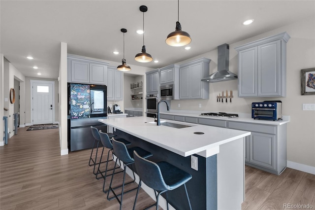 kitchen featuring gray cabinets, sink, a kitchen island with sink, stainless steel appliances, and wall chimney exhaust hood