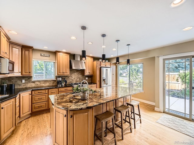 7826 S Niagara Way, Centennial, CO 80112 - kitchen featuring stainless steel appliances, wall chimney range hood, light wood finished floors, a kitchen breakfast bar, and decorative backsplash