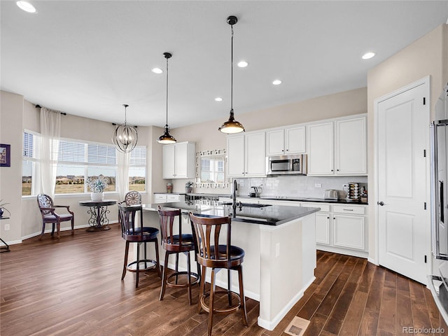 kitchen featuring stainless steel microwave, dark wood finished floors, a kitchen island with sink, white cabinetry, and recessed lighting