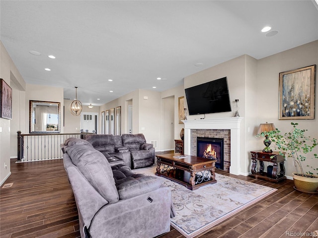 living room featuring dark wood-type flooring, a fireplace, baseboards, recessed lighting, and a chandelier