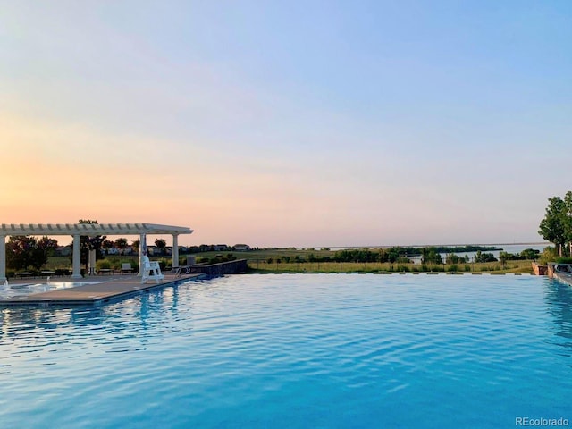 pool at dusk featuring a pergola, a water view, and a community pool