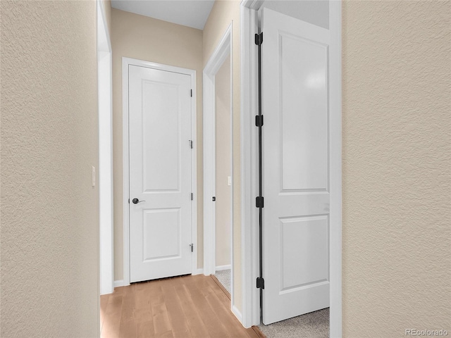 hallway featuring a textured wall, light wood finished floors, and baseboards