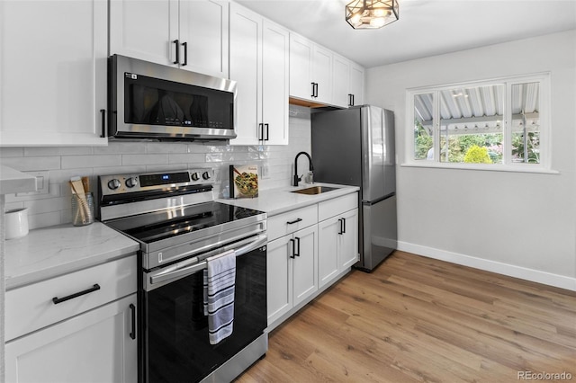 kitchen featuring sink, appliances with stainless steel finishes, light stone counters, light hardwood / wood-style floors, and white cabinets