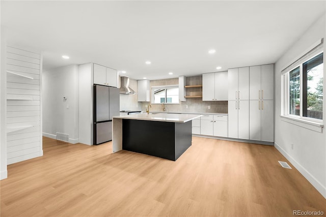 kitchen featuring wall chimney range hood, a kitchen island, white cabinets, and stainless steel fridge