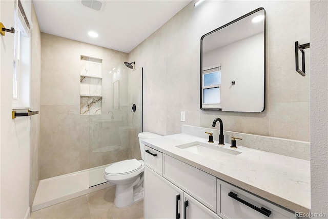 bathroom with a tile shower, toilet, vanity, and tile walls