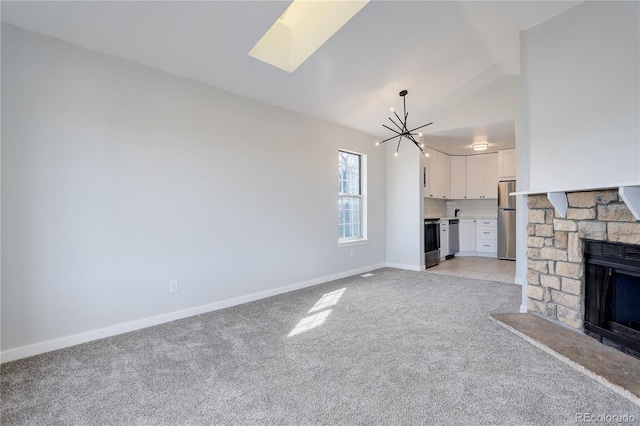 unfurnished living room featuring light carpet, a notable chandelier, a stone fireplace, and vaulted ceiling with skylight