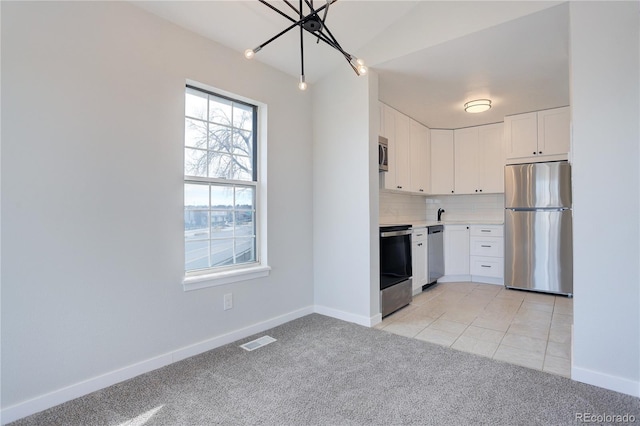 kitchen with tasteful backsplash, white cabinetry, appliances with stainless steel finishes, and light colored carpet