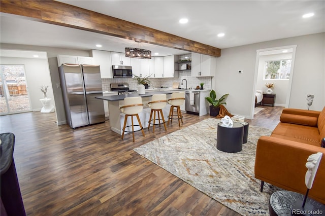 living room featuring beamed ceiling, a wealth of natural light, dark wood-type flooring, and sink