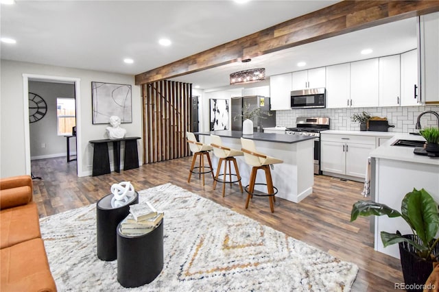 kitchen featuring beam ceiling, a center island, sink, stainless steel appliances, and white cabinets