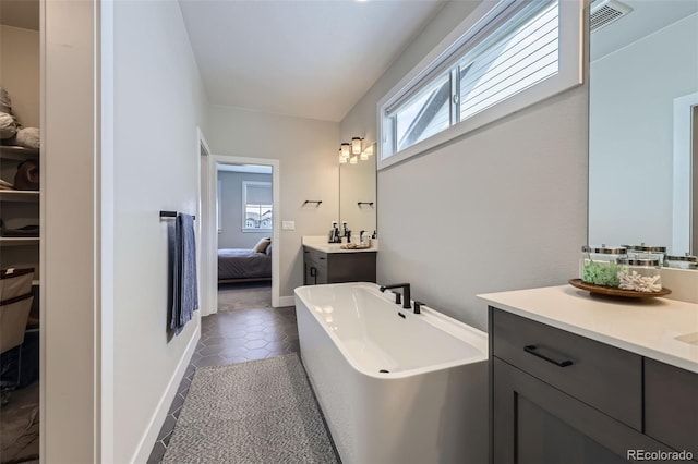 ensuite bathroom with healthy amount of natural light, a freestanding tub, vanity, and tile patterned flooring