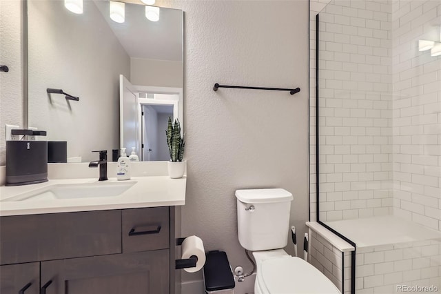 full bath featuring toilet, vanity, tiled shower, and a textured wall