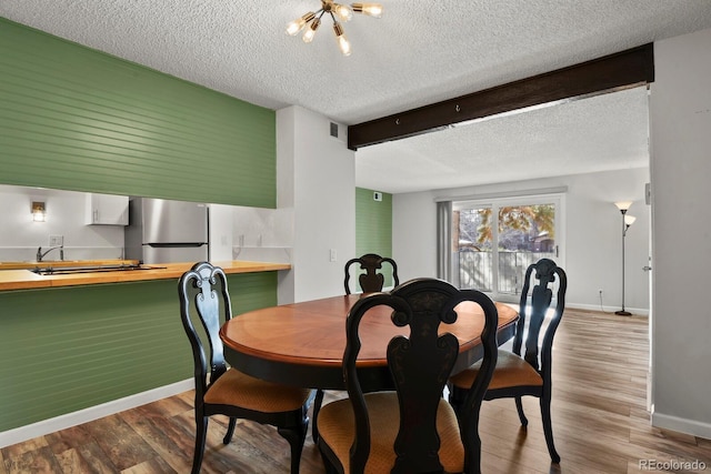 dining room with beamed ceiling, a notable chandelier, wood-type flooring, and a textured ceiling