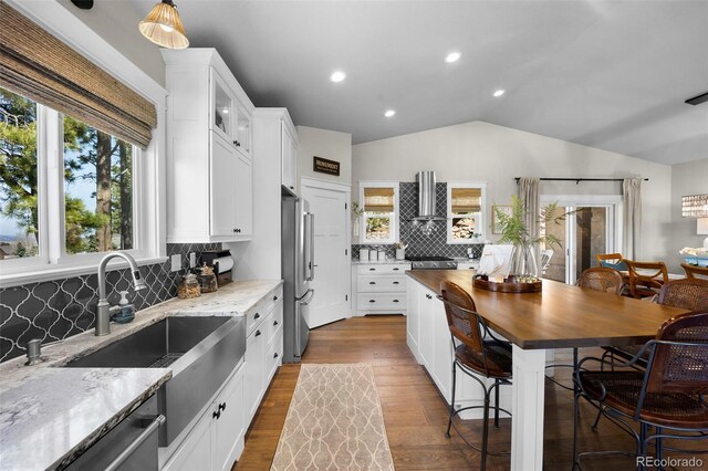 20243 High Pines Dr, Monument, CO 80132 - kitchen with wall chimney range hood, appliances with stainless steel finishes, wood counters, tasteful backsplash, and lofted ceiling