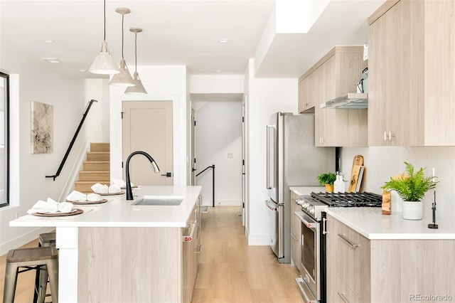 kitchen with sink, light brown cabinets, high end range, hanging light fixtures, and a center island with sink