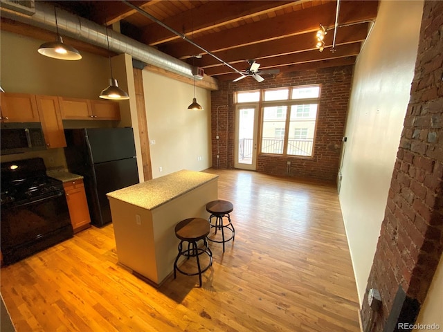 kitchen with brick wall, decorative light fixtures, a kitchen bar, a center island, and black appliances