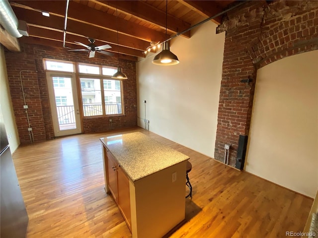 kitchen featuring light stone counters, hanging light fixtures, light wood-type flooring, ceiling fan, and brick wall