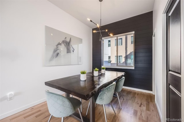 dining room featuring light wood-type flooring, baseboards, and wood walls