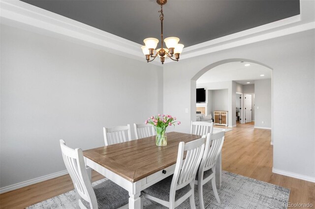 17378 W 78th Dr, Arvada, CO 80007 - dining area featuring arched walkways, a chandelier, light wood finished floors, a raised ceiling, and baseboards