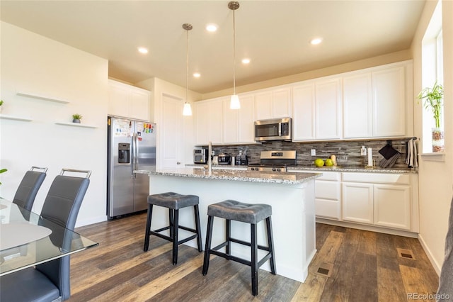 kitchen with a kitchen island with sink, white cabinetry, appliances with stainless steel finishes, light stone countertops, and decorative light fixtures