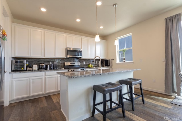 kitchen with a center island with sink, appliances with stainless steel finishes, white cabinets, and pendant lighting